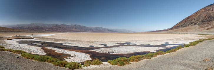 Panorama of the Bad Water Basin area, in Death Valley, with some tourists walking along the walkways, on a smoky day