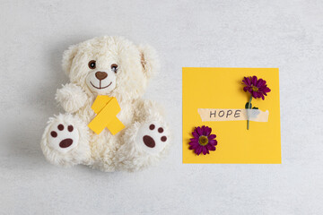Yellow ribbon, teddy bear and flowers with the word hope.