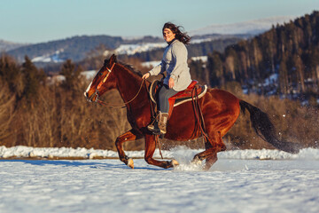 Romantic equestrian scene: A young woman ride her horse in gallop through a snowy winter landscape...