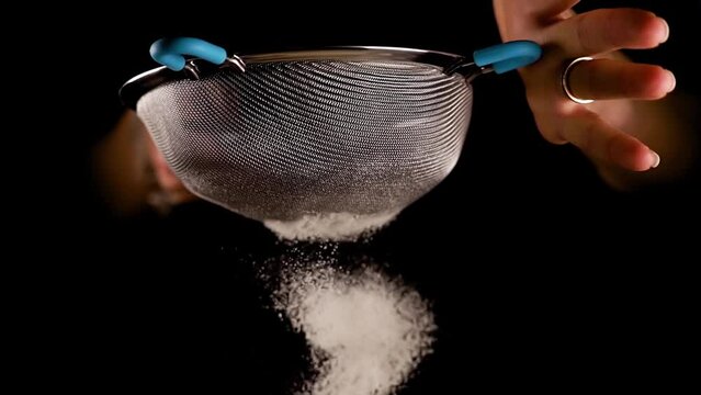 Woman hands sift white wheat flour shaking contemporary metal sieve on deep black background extreme close view slow motion