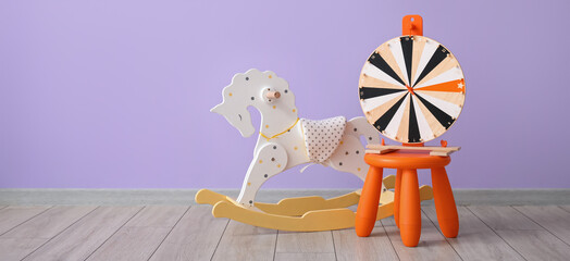 Rocking horse and stool with wheel of fortune near lilac wall in room