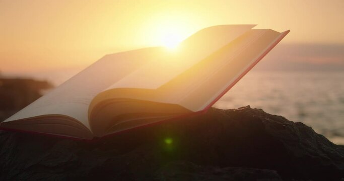 Open book illuminated by sunlight at sunset by ocean. World poetry day.