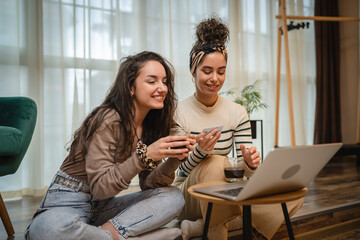 Fototapeta premium Two friends or sisters or girlfriends are using laptop to do shopping online in their apartment