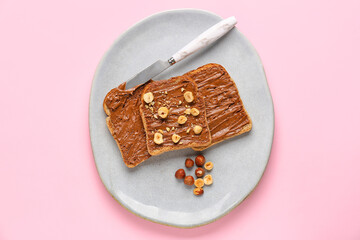 Plate of tasty toasts with hazelnut butter and nuts on pink background