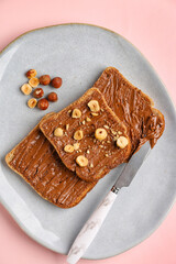 Plate of tasty toasts with hazelnut butter and nuts on pink background, closeup