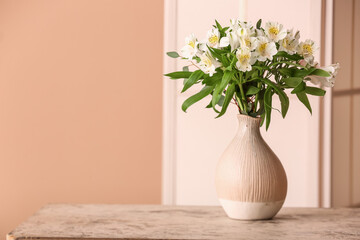 Vase with bouquet of alstroemeria flowers on table near beige wall