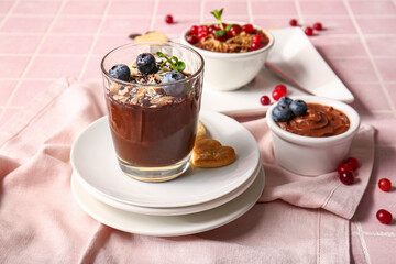 Bowls and glass of delicious chocolate pudding with berries and almond on pink tile table