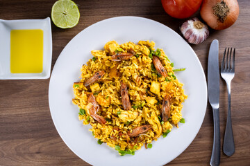 Classic Spanish dish. Spanish paella with prawns, octopus, squid, mussels, onion, tomato, garlic, olive oil and lemon. Assembled on white plate on wooden background.