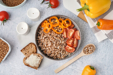 Bowl of tasty buckwheat porridge with fresh vegetables and bread on grey table