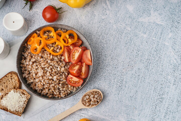 Bowl of tasty buckwheat porridge with fresh vegetables and bread on grey table