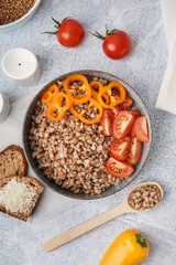 Bowl of tasty buckwheat porridge with fresh vegetables and bread on grey table