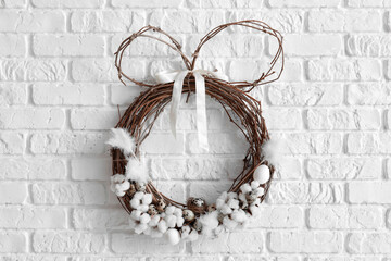 Easter wreath with cotton flowers and quail eggs on white brick wall