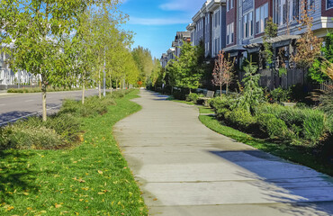 Green city street with walkway in residential area in sunny summer day. Neighborhood modern houses with trees and green grass in BC, Canada. Canadian modern residential architecture.