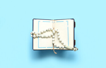 Open Koran with prayer beads for Ramadan on blue background