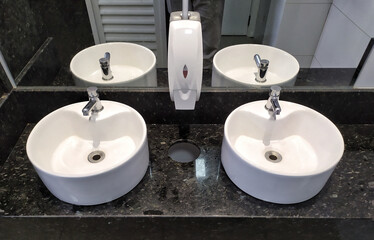 Fototapeta premium Two white sinks with silver faucets above and a soap dish next to the mirror in the bathroom