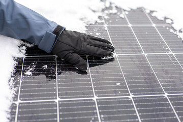 Getting electricity with solar panels in winter.Hands clear snow from solar panels.renewable energy...