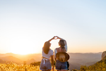 Two happy female friends making heart shape with their hands with sunset in the background.