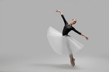 Young ballerina practicing dance moves on light grey background. Space for text - obrazy, fototapety, plakaty