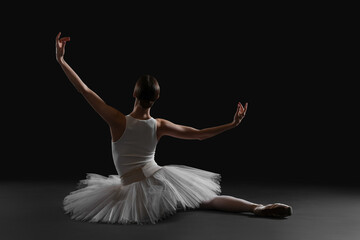 Young ballerina sitting on split against black background, back view © New Africa