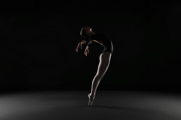 Fototapeta na wymiar Young ballerina practicing dance moves on black background