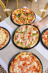 Restaurant table with five delicious assorted pizzas including pepperoni, vegetable, seafood and more. Irresistible aroma of freshly baked pizza.