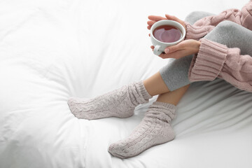 Woman with cup of tea wearing warm socks in comfortable bed, closeup. Space for text