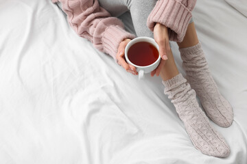 Woman with cup of tea wearing warm socks in comfortable bed, closeup. Space for text