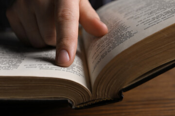 Naklejka premium Man reading holy Bible at wooden table, closeup