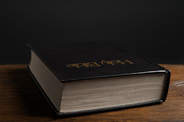 Hardcover Bible on wooden table against black background, closeup