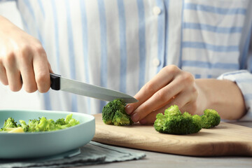 Woman cutting boiled broccoli at table, closeup. Child's food