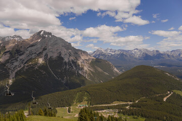 Fototapeta na wymiar Mountain landscape - coniferous forest, beautiful blue sky with clouds. Summer tourism - ski lift to the mountain. Banff, Alberta, Canada. Rocky Mount