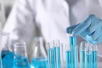 Scientist taking test tube with light blue liquid in laboratory, closeup. Space for text