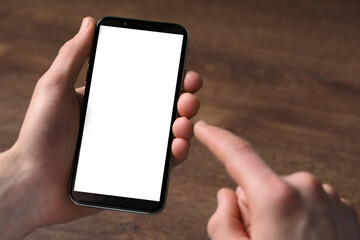 Man holding smartphone with blank screen at wooden table, closeup. Mockup for design