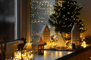 Beautiful decorative houses, baubles and small Christmas tree on window sill indoors