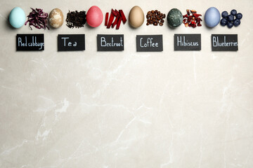 Easter eggs painted with natural organic dyes and labels on light grey table, flat lay. Red cabbage, tea, beetroot, coffee beans, hibiscus, blueberries used for coloring. Space for text