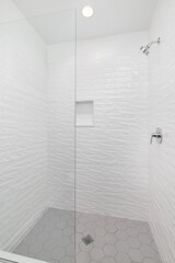 A walk-in shower with white wavy subway tiles, a grey hexagon tiled floor, and a chrome shower head.