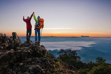 Successful two hiker standing with raised hands on top mist mountain sunny morning sunrise time.