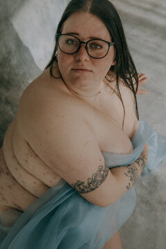fat woman with glasses and black hair looking up at camera with body exposed