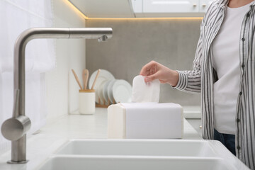 Woman taking paper towel from package in kitchen, closeup