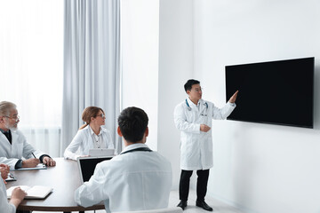 Team of doctors listening to speaker report near tv screen in meeting room. Medical conference