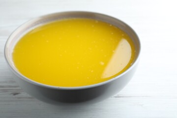 Clarified butter in bowl on white wooden table, closeup