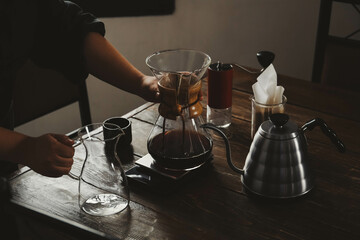 Barista with coffee maker and jug at wooden table in cafe, closeup