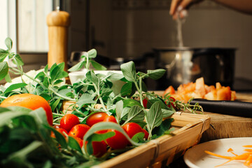 Organic vegetables in a basket, tomatoes and leaves, pot cooking in the background