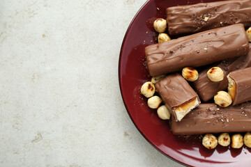 Tasty chocolate bars with caramel and nuts on light grey textured table, top view. Space for text