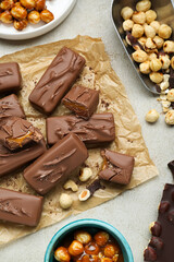 Delicious chocolate candy bars and nuts on light table, flat lay