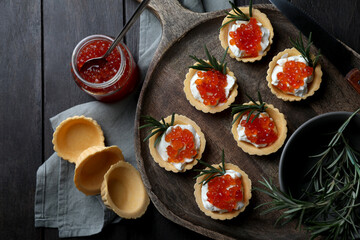 Delicious tartlets with red caviar and cream cheese served on wooden table, flat lay