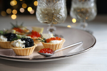 Delicious tartlets with red and black caviar served on white wooden table against blurred festive...