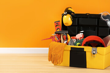 Box with different tools for repair on floor near orange wall, space for text