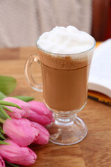 Glass of delicious cocoa and pink tulips on wooden table