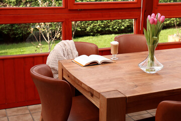 Glass of delicious cocoa, pink tulips and book on wooden table at terrace